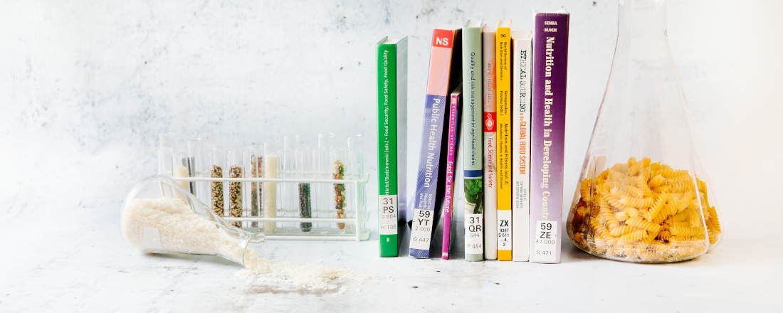Various books on the subject of food and nutrition are lined up next to a series of test tubes with legumes, next to them is a bottle of rice
